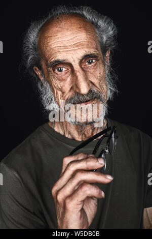 close up portrait of senior man in glasses taking off glasses, old age concept isolated black background. studio shot Stock Photo
