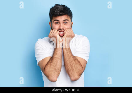 puzzled fearful handsome bearded man keeping fists near his chin, cheeks looks with surprsied expression, being scared to hear horrified news, isolate Stock Photo