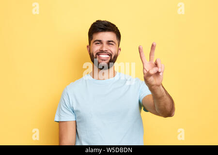 smiling cheerful young man showing two fingers up, victory sign. close up portrait, studio shot, body language, success, luck, happiness Stock Photo