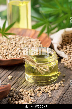 Composition with hemp products. Cannabis oil, seeds and green leaves on old wooden board. Stock Photo