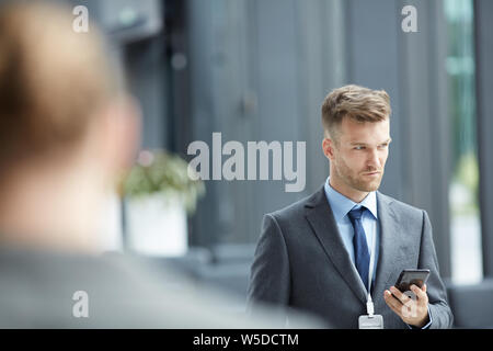 Serious thoughtful handsome representative with badge standing in conference lobby and using smartphone Stock Photo