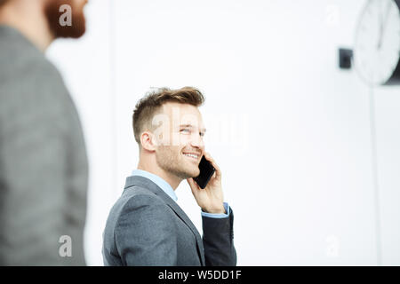Smiling handsome young businessman with stubble talking on mobile phone while walking over lobby Stock Photo