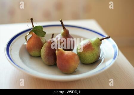 five pears in a white plate on a light wooden table. Stock Photo