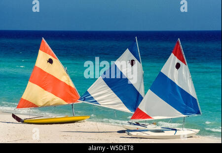 Three small sailboats rest at the water's edge while waiting for vacationers on the Gulf of Mexico coast to rent them at Panama Beach in the panhandle of Florida, USA. Brand-named 'Sunfish' by the boat builder, the one-person fiberglass sailing craft are easily identified by the American company's emblem on their bright striped sails. With a broad flat hull and triangular sail, these light-weight vessels are easy to maneuver and are a favorite of novice sailboaters. Since being introduced in 1952, Sunfish have become popular throughout the world and even have international racing competitions. Stock Photo