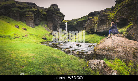 Woman sat looking at waterfall in Skógar Iceland Stock Photo