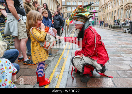 Glasgow, Scotland, UK. 28th July 2019. After heavy rain showers causing some entertainment to cancel, OCEANALLOVER, an international street entertainment theatre, took advantage of a brief respite in the rain and entertained the crowds in Brunswick Street with their play 'Transfigured'. Picture is of actor ANNA PORUBCANSKY interacting with LEAH DOWNIE, aged 4, from Glasgow Credit: Findlay/Alamy Live News Stock Photo