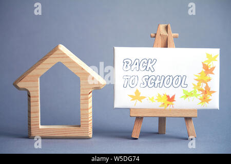 A wooden figure of house on gray background and white board on miniature easel with the words Back to School, selective focus Stock Photo