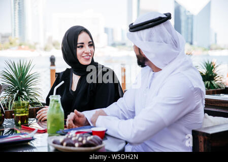 Happy couple spending time in Dubai. man and woman wearing traditional clothes having a conversation in a cafe Stock Photo