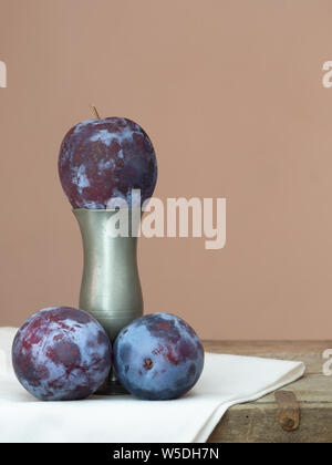 Three dark red, purple plums one on vase pedestal. Stock Photo