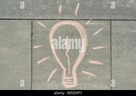 Abstract image drawing of light bulb written on grey sidewalk. Stock Photo