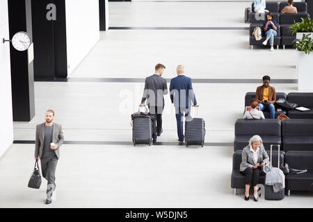 Above view of modern businessmen in formalwear carrying wheeled suitcases while crossing airport waiting area Stock Photo