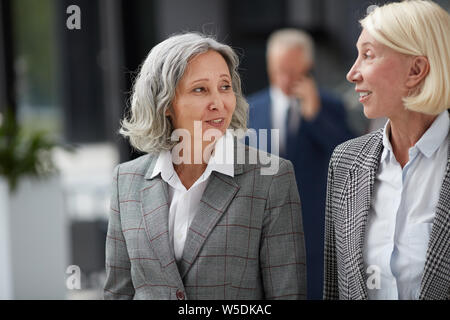 Smiling Asian lady with short gray hair looking at colleague while talking to her about business Stock Photo