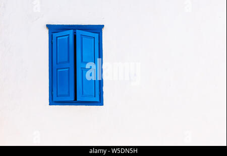 White wall with blue window and closed shutters. Greek style. Stock Photo