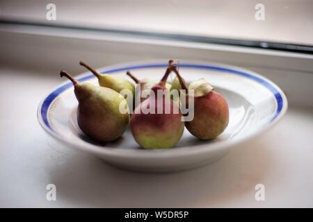 five ripe pears in a plate on the windowsill Stock Photo
