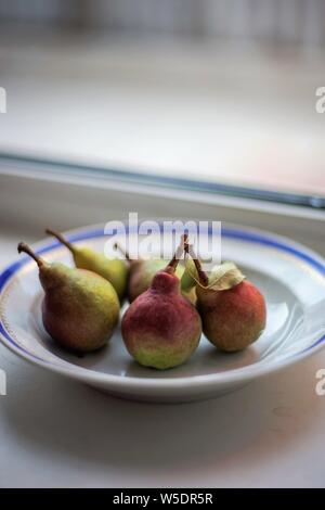 five ripe pears in a plate on the windowsill Stock Photo