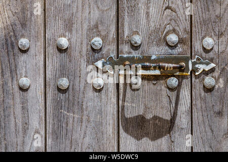 Handle of a weathered wooden door and it's shadow forming an abstract face with a mustache and two rivets as eyes or a cow's face - head-on view Stock Photo