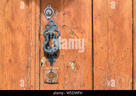 Metal doorknocker on an aged wooden door with cracked paint (close-up, landscape format) Stock Photo