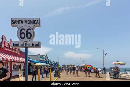 Los Angeles California USA. May 30, 2019. Santa Monica pier and Route 66 End of the trail, white color  sign. People walking at pier, blue sky backgro