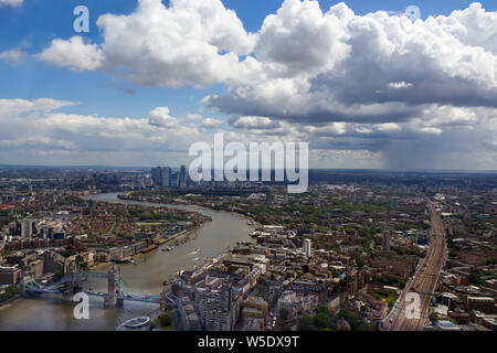 View form The Shard looking east along the Thames towards docklands. Looking along the train lines from London Bridge, a distant rain storm is visible. Stock Photo