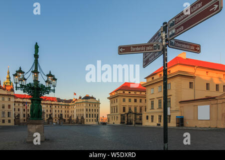 Hradcany Square in front of the entrance to Prague Castle with signs. Historically decorated fountain with the Schwarzenberg Palace in the evening in Stock Photo