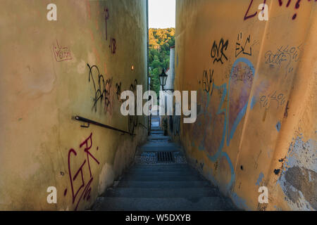 Narrow alley with steps and railing from Hradcany Square down to Prague's Old Town. Trees and sky on the horizon and yellow walls during the evening s
