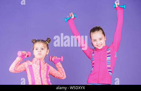 Toddler repeat exercise after sister. Sport exercises for kids. Healthy upbringing. Sporty babies. Following her sister. Girls cute kid exercising with dumbbells. Motivation and sport example concept. Stock Photo