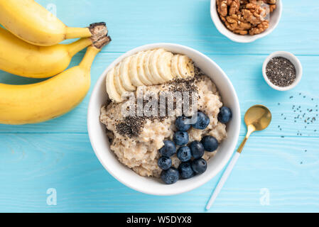 Bowl of oatmeal porridge with banana, blueberry and chia seeds on blue background. Table top view Stock Photo
