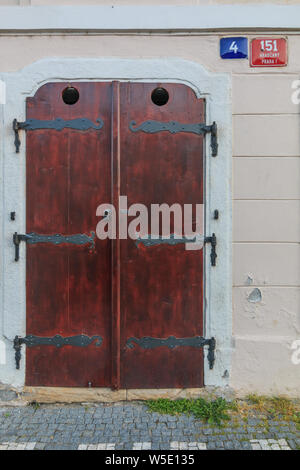 Historic closed wooden door on a building wall. Brown door with black metal fittings. bright wall with street sign and house number. walkway with pavi Stock Photo