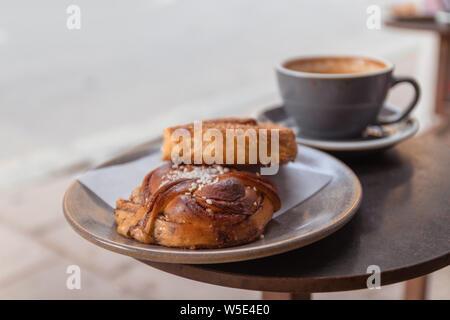Cup of coffee and bun with cinnamon lying on the table in cafe in a street cafe. Stock Photo
