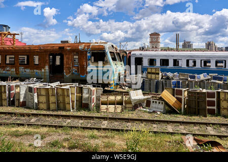 Battered old electric train and wagons on the railway tracks in the railroad depot on the background of the sunny blue sky with white clouds. There ar Stock Photo