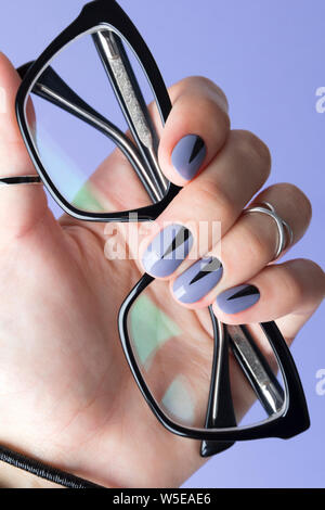 Female hand with fashionable manicure holding black glasses at purple background Stock Photo