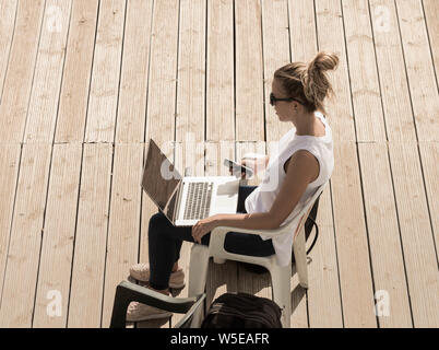 Woman using laptop on beach boardwalk. Stock Photo