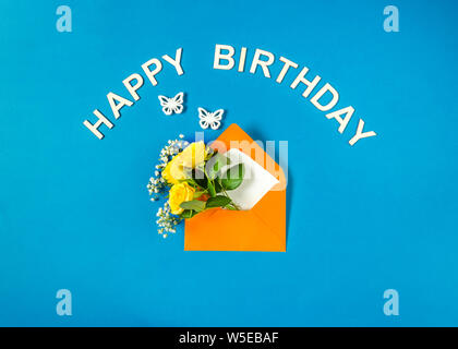 Yellow roses and white Gypsophila in orange envelope close-up on cyan background. Two white butterflies. Text Happy Birthday. Top view, flat lay. Temp Stock Photo