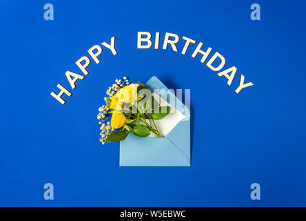 Yellow roses and white Gypsophila in blue envelope close-up on blue background. Text Happy Birthday, wooden letters. Top view, flat lay. Template for Stock Photo