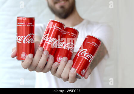 KHARKIV, UKRAINE - JULY 15, 2019: Smiling man holding many non-alcoholic Coca-Cola aluminium tin cans in garage interior. Coca Cola is the most famous Stock Photo