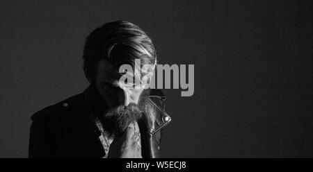 brooding bearded hipster in a leather jacket looking somewhere to the side. isolated on black background Stock Photo