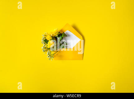 Open envelope with yellow roses and small white flowers Gypsophila on yellow background. Top view, flat lay. Concept of sending greetings, love, frien