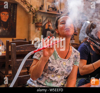 A woman blows smoke from her hookah pipe inside a restaurant in Amman, Jordan. Stock Photo