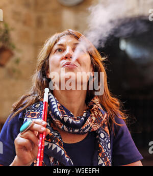 A woman blows smoke from her hookah pipe inside a restaurant in Amman, Jordan. Stock Photo