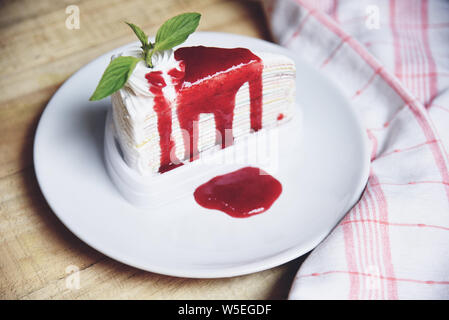 Crape cake slice with strawberry sauce on white plate on wooden background / Piece of cake rainbows with whipped cream Stock Photo