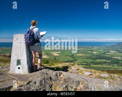 A lone female walker at the top of Garn Fadryn checks a map while facing Nefyn on the Llyn Peninsula, Gwynedd, Wales, UK Stock Photo