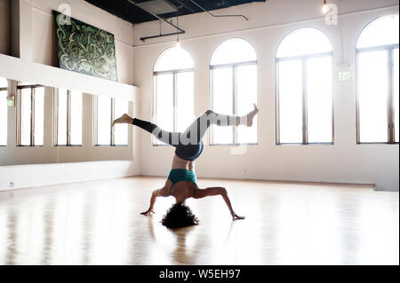Woman practicing yoga in an extraordinary headstand with a twist. Beautiful window light in an old ballet studio. Stock Photo