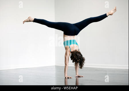 Woman practicing yoga. She is practicing advanced poses in a beautiful simple white wall studio interior. Stock Photo