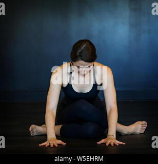 A young beautiful brunette white woman does yoga poses against a dark background. Stock Photo