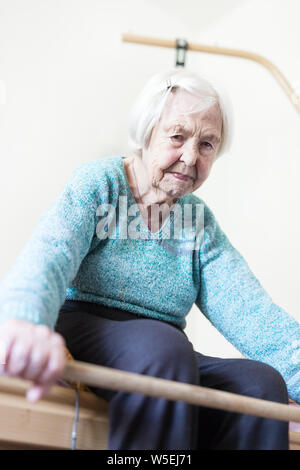 Elderly 96 years old woman exercising with a stick sitting on her bad. Stock Photo