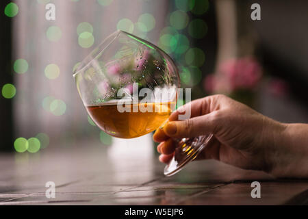 Female hand holding glass of cognac. Relaxation concept. Snifter of brandy in elegant glass with space for text. Strong alcoholic drink. Stock Photo