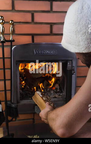 Comfort interior with closed burning fireplace. A man throws wood in the fireplace Stock Photo