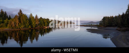 Beautiful Panoramic View of a river joining the ocean in a small town during a cloudy and sunny summer sunrise. Taken at Port Renfrew, Vancouver Islan Stock Photo