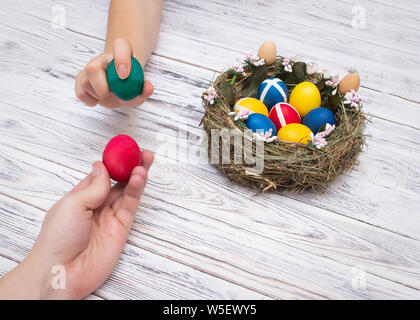 two people holding colorful chicken easter eggs on a white wooden background concept of the game and tradition in egg fight, hands, nest, Christianity Stock Photo