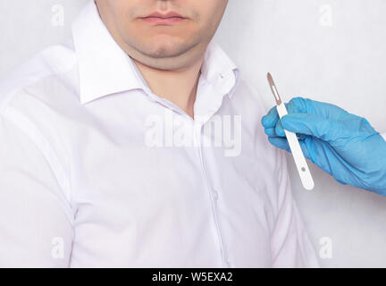A doctor holds a scalpel on the background of a patient with a double chin, plastic surgery and plastic, close-up Stock Photo